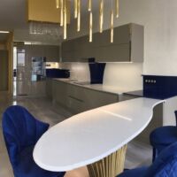 Благодаря светлому кварциту Caesarstone 5110 Alpine Mist на основной столешнице и барной стойке интерьер кухни выглядит изысканно-праздничным. А синий кварцит Technistone Starlight Sapphire на боковых деталях столешницы и стеновых панелях - как глоток морозной свежести, ворвавшейся в распахнутое окно. Столешницы из кварцита Caesarstone и Technistone. Фото 1